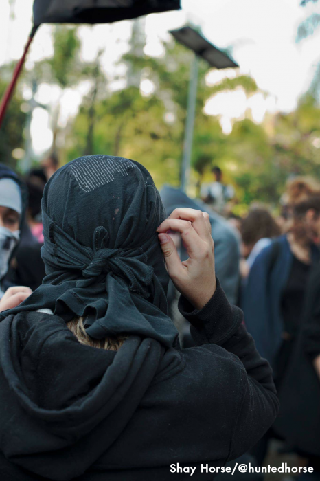 A member of the black bloc adjusts their mask before the protests began. The black bloc is a tight not group and would assist each other in "Bloc-Ing" up. Meaning wearing the trade mark all black clothing of a Black Bloc. 